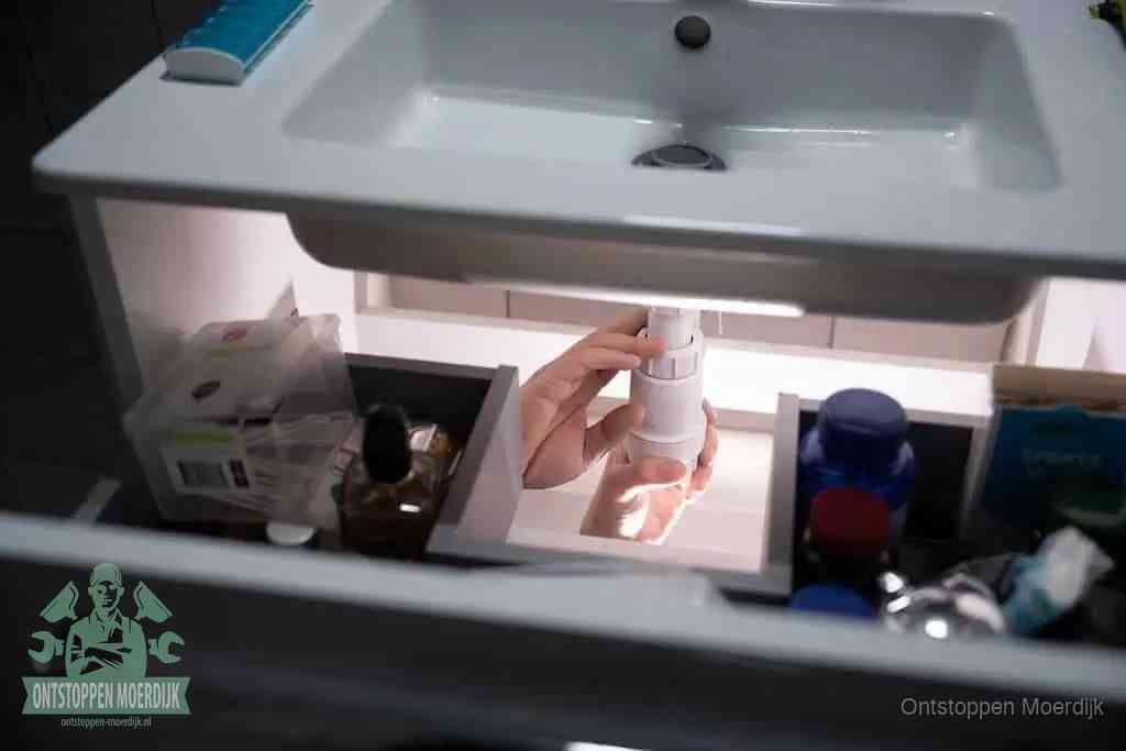 Een pompfles met zeep boven een wastafel, de heet water en afwasmiddel-methode om een vetprop in de afvoer los te maken in Moerdijk