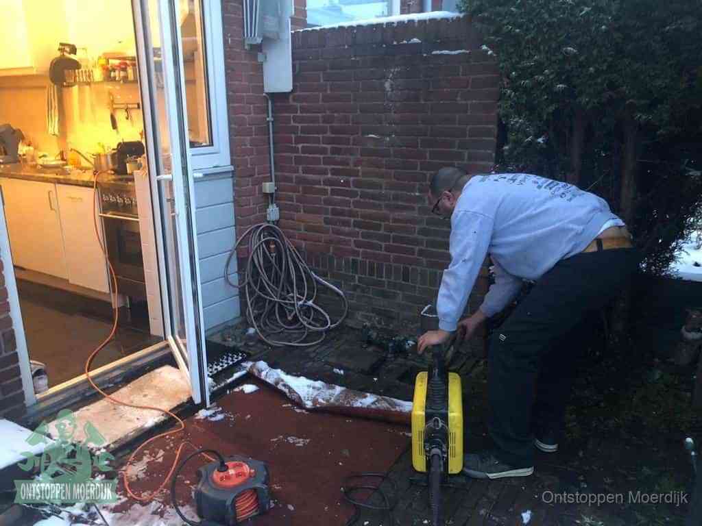 Een monteur werkt buiten bij een open riool-/grondput met een elektrische ontstoppingsmachine om een verborgen afvoerprobleem op te sporen in Moerdijk