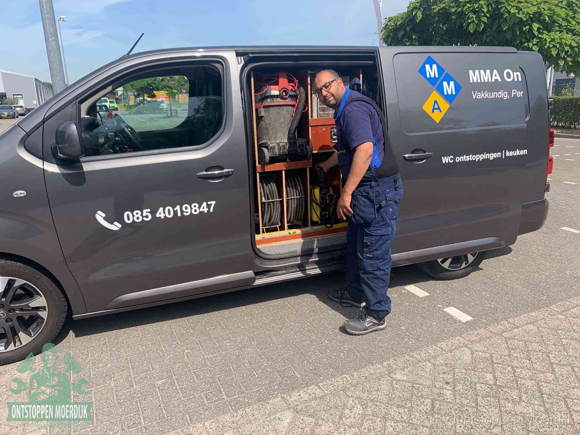 Een monteur bij de open schuifdeur van zijn bedrijfsbus op een parkeerplaats, klaar om de oorzaak van terugkerende afvoerverstoppingen aan te pakken in Moerdijk