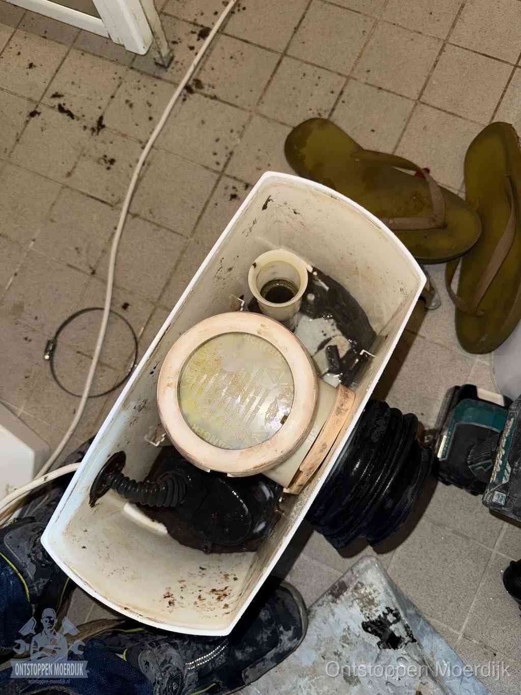 Een gedemonteerde toiletpot op de vloer met ontstoppingsveer en gereedschap ernaast, het verwijderen van een vastzittend voorwerp uit de wc in Moerdijk
